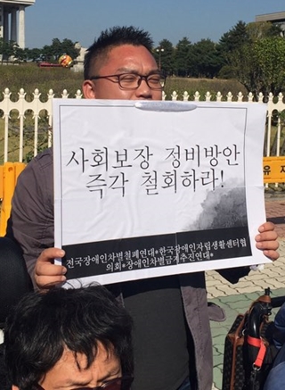 28일 열린 기자회견에서 한 활동가가 '사회보장 정비방안 즉각 철회하라'라는 피켓을 들고 있다. ⓒ에이블뉴스