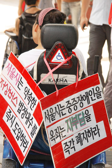 한 장애인의 휠체어에 서울시 장애인활동지원 추가자부담 폐지와 이동권 보장을 촉구하는 플랜카드가 걸려 있다. ⓒ에이블뉴스 